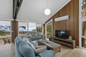 A modern living room with a large TV, comfortable seating, and a view of the outdoors.