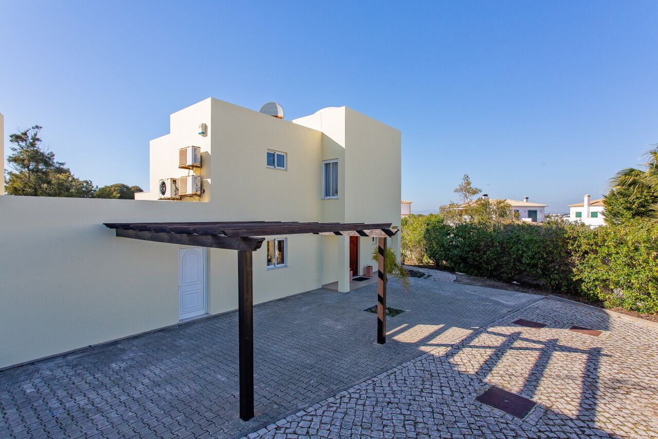 A modern building with a covered outdoor area, a paved courtyard, and a clear sky.