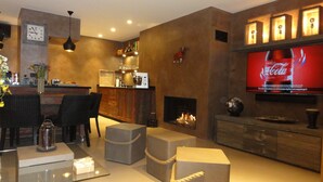 A modern living room with a fireplace, a television displaying a Coca-Cola ad, and a bar area with a clock and decorative items. - Upscale apartment in a quiet location, accessible for disabled people (Hyères)