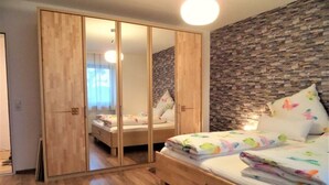 A bedroom with a wooden bed, a wardrobe with mirrored doors, and a stone-textured wall.