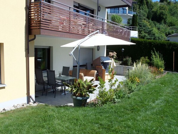 Une terrasse avec des meubles d’extérieur, une plante en pot et une vue sur un immeuble d’habitation.