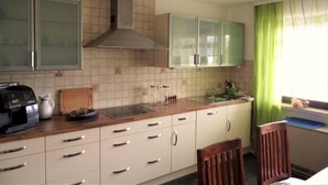 A compact kitchen with white cabinets, a stove, and a window with green curtains.