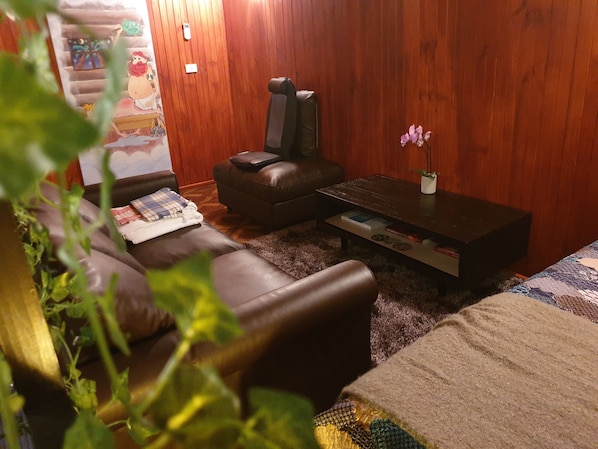 A cozy living room with a leather sofa, a brown leather chair, a small coffee table with books, and a wall-mounted TV.