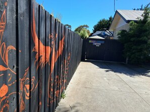 Un espace délimité par une clôture, avec un chemin bien défini menant à un bâtiment sur lequel est apposée une pancarte indiquant un espace de stationnement.