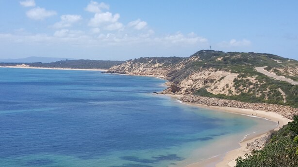 Un paysage côtier avec une plage, des falaises rocheuses et une mer bleue et limpide.