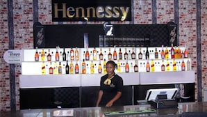 A bar area with a Hennessy sign, a variety of liquor bottles, and a counter with a payment terminal. - KINGS PALACE HOTEL & LOUNGE (Ipaja)