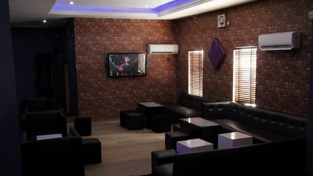 A modern lounge with a brick wall, leather seating, and a flat-screen TV. - KINGS PALACE HOTEL & LOUNGE (Ipaja)