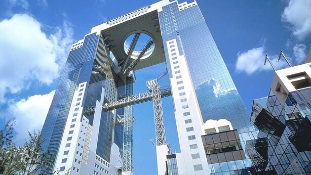 Un gratte-ciel moderne, doté d’un élément circulaire distinctif au sommet, et entouré d’autres immeubles de grande hauteur.