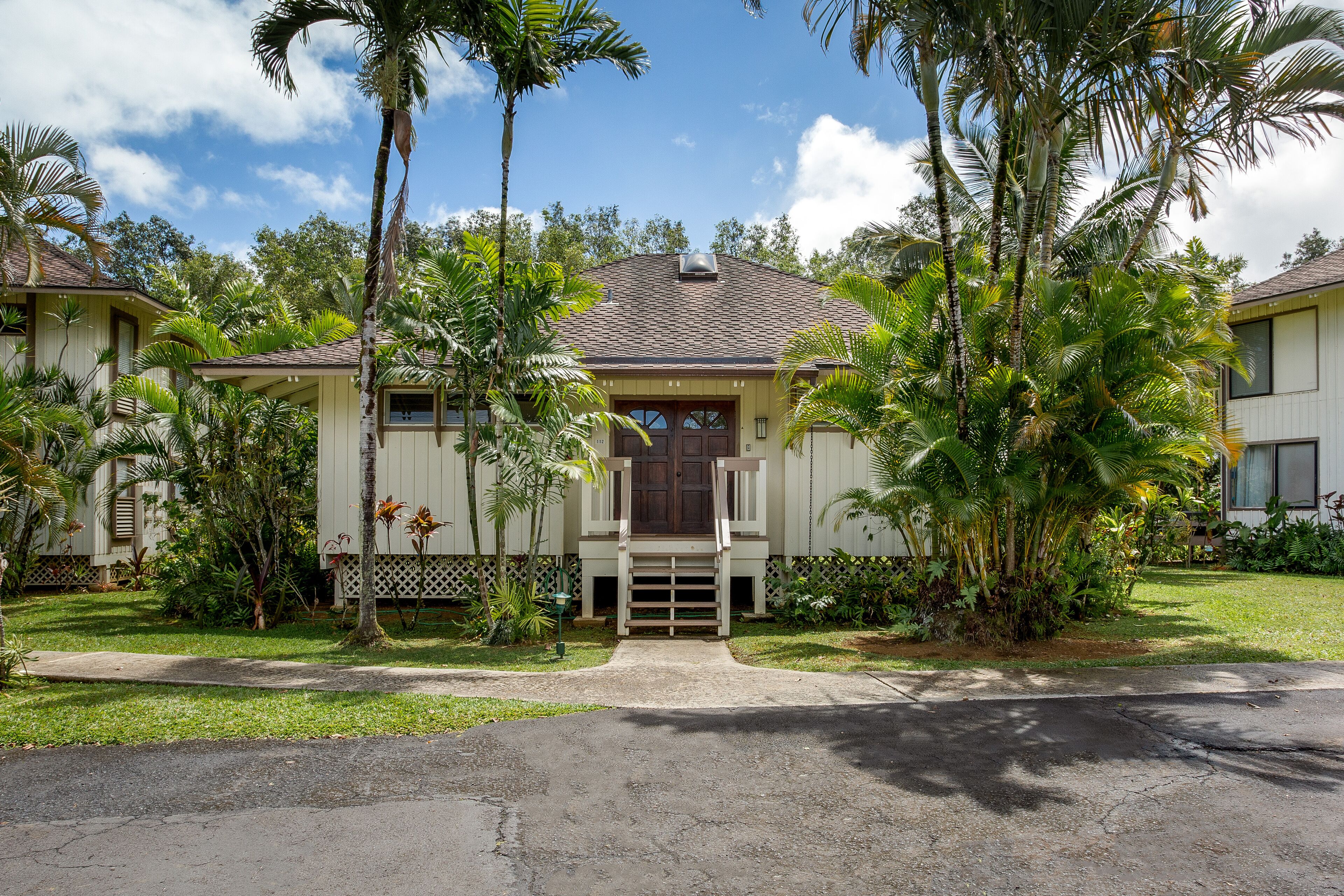 A two-story house with a front porch, surrounded by palm trees and a well-maintained lawn.