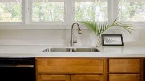 A kitchen with a stainless steel sink, wooden cabinets, and a window with a view of greenery. - Quaint stand-alone cottage - 2 bedroom 2 bath (Princeville)
