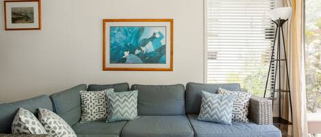 A sectional sofa with patterned cushions, a framed abstract painting, and a floor lamp.