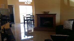 Una sala de estar con chimenea, ventilador de techo y comedor con sillas y mesa.