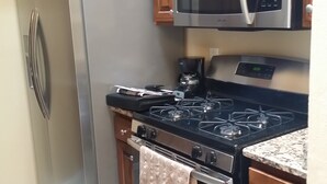 Una cocina con refrigerador de acero inoxidable, microondas, estufa a gas y alacenas de madera.