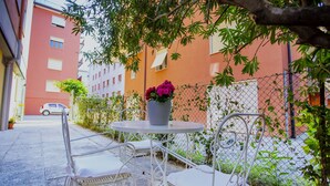 A courtyard with a round table and white chairs, surrounded by a chain-link fence and greenery. - Laguna Boutique Apartments | 2-bedroom with patio & parking in Venice Mestre (Venezia)