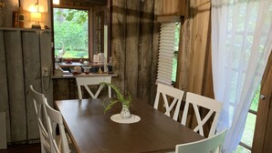 Ein Essbereich mit Holztisch und weißen Stühlen, einem Deckenventilator und Blick auf Grünflächen.