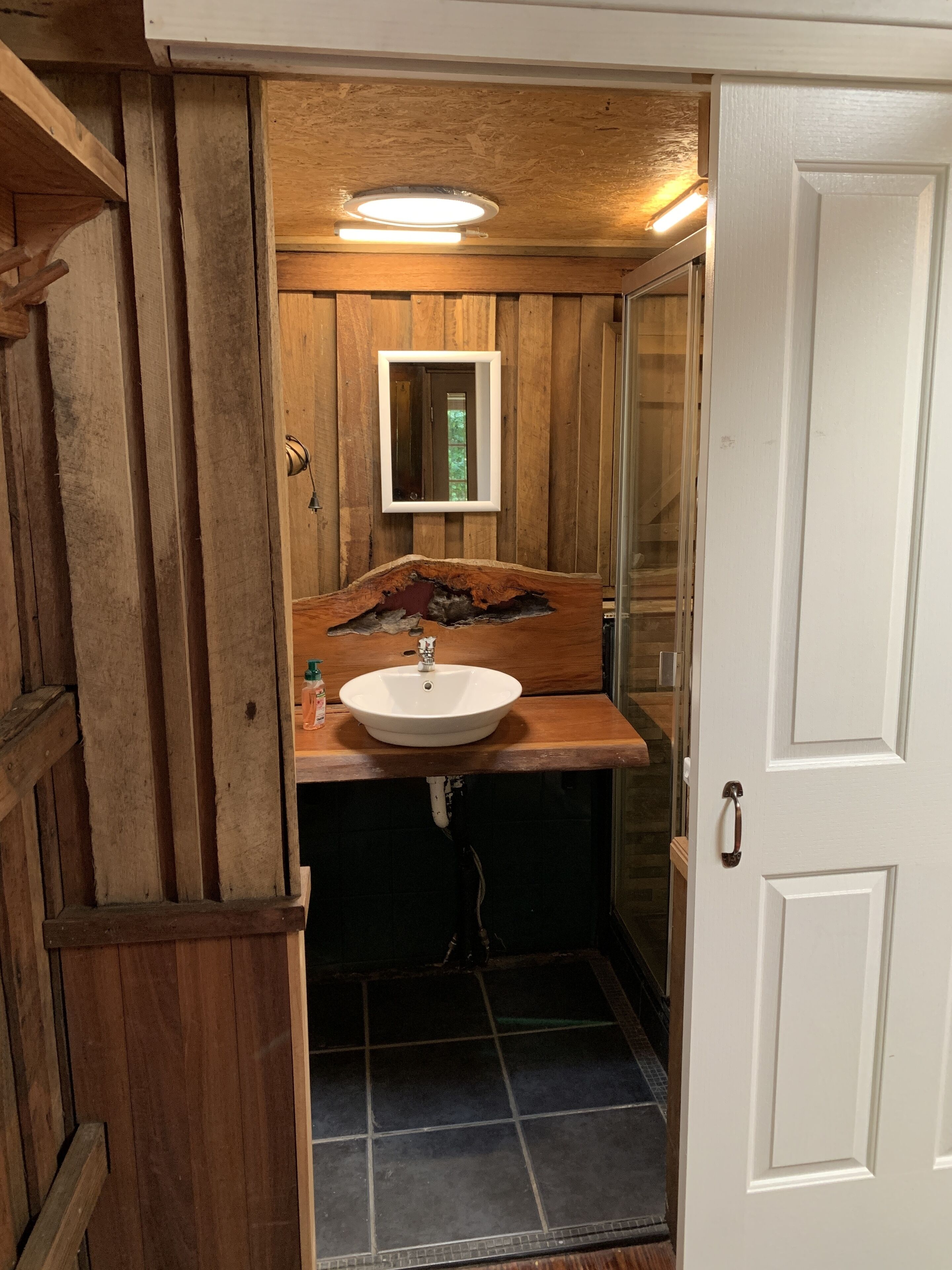 Un baño con revestimiento de madera, un lavamanos blanco, un espejo y una puerta.