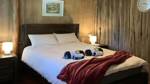 Ein Bett mit Holzrahmen, weiße Bettwäsche, zwei Nachttischlampen, eine Uhr an der Wand und ein gerahmtes Bild über dem Bett.
