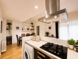 A compact kitchen with a built-in washing machine, a stove, and a dining area with chairs and a table.