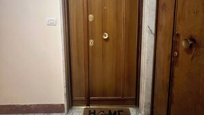 Puiset ovet, joiden edessä on kynnysmatto, jossa lukee ”KOTI”, ja lattia on marmoria.