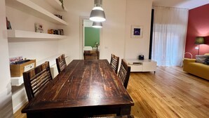 Ruokailutila, jossa on puinen pöytä ja tuolit, riippuvalaisin ja valkoinen kaappi.