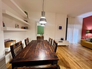 Un'area pranzo con tavolo e sedie in legno, una lampada a sospensione e un armadietto bianco.