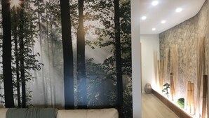 Une pièce dont un mur est décoré d’une fresque sur le thème de la forêt, avec un canapé agrémenté d’un plaid vert et un élément décoratif mural en bambou.
