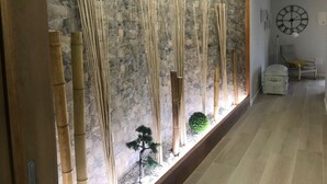 Une pièce avec un mur en pierre, une horloge, une chaise et une petite plante.