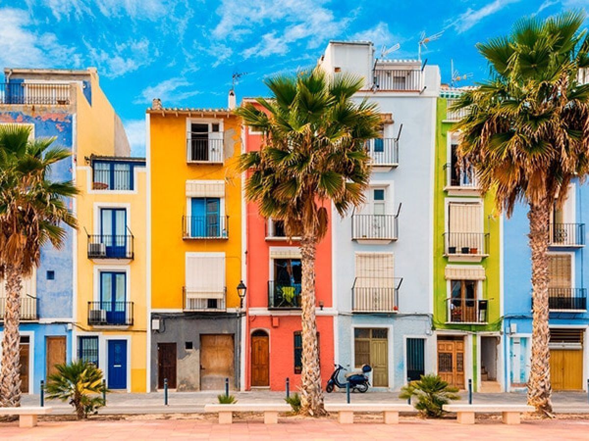Una hilera de edificios coloridos con balcones, palmeras y una moto estacionada en frente.