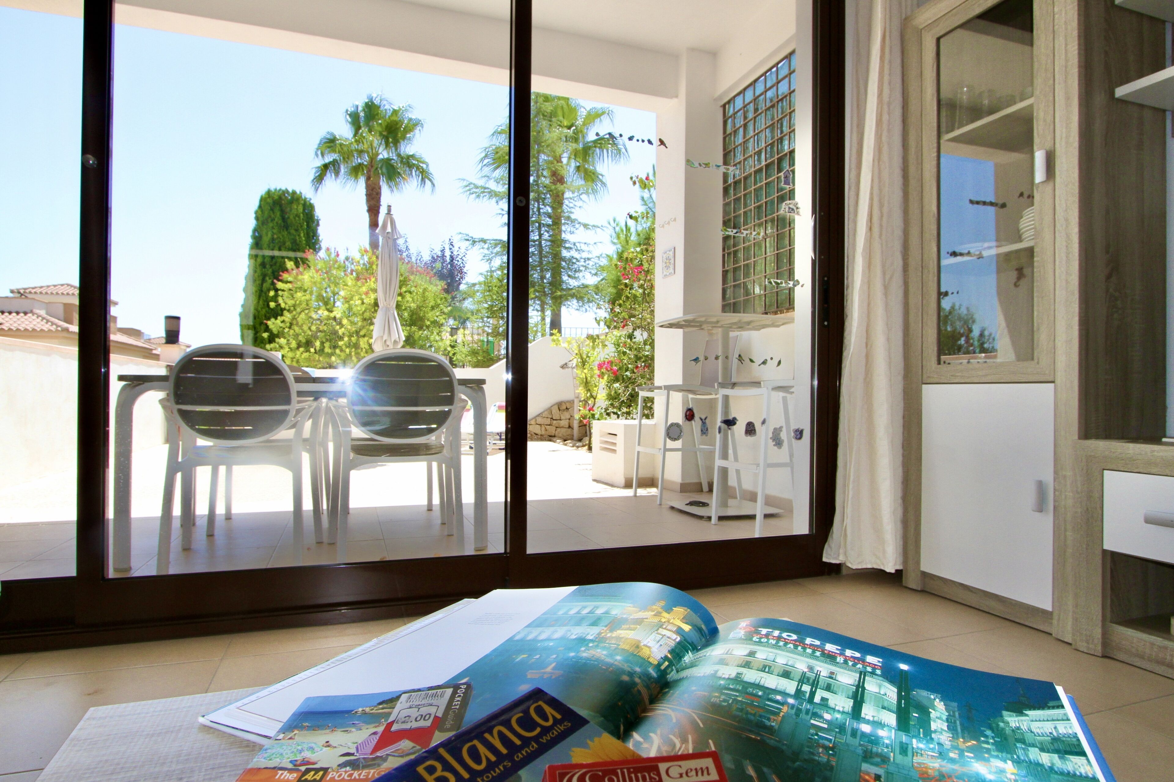 Una habitación con un ventanal grande, una mesa con sillas y una revista en el suelo.