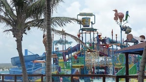 Een kleurrijk waterpark met diverse speelconstructies en een strandgedeelte met palmbomen.
