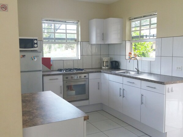 A compact kitchen with white cabinets, a gas stove, a microwave, and a sink. - Beautiful and cozy vacation home, with pool and hot shower. For 4 people. (Oranjestad)