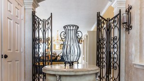 A grand hallway with a marble floor, a central table with a vase, and ornate black metal gates. - ENJOY RESORT  STYLE LUXURY ACCOMMODATIONS AT THE ESTATE HOME (Mansfield)