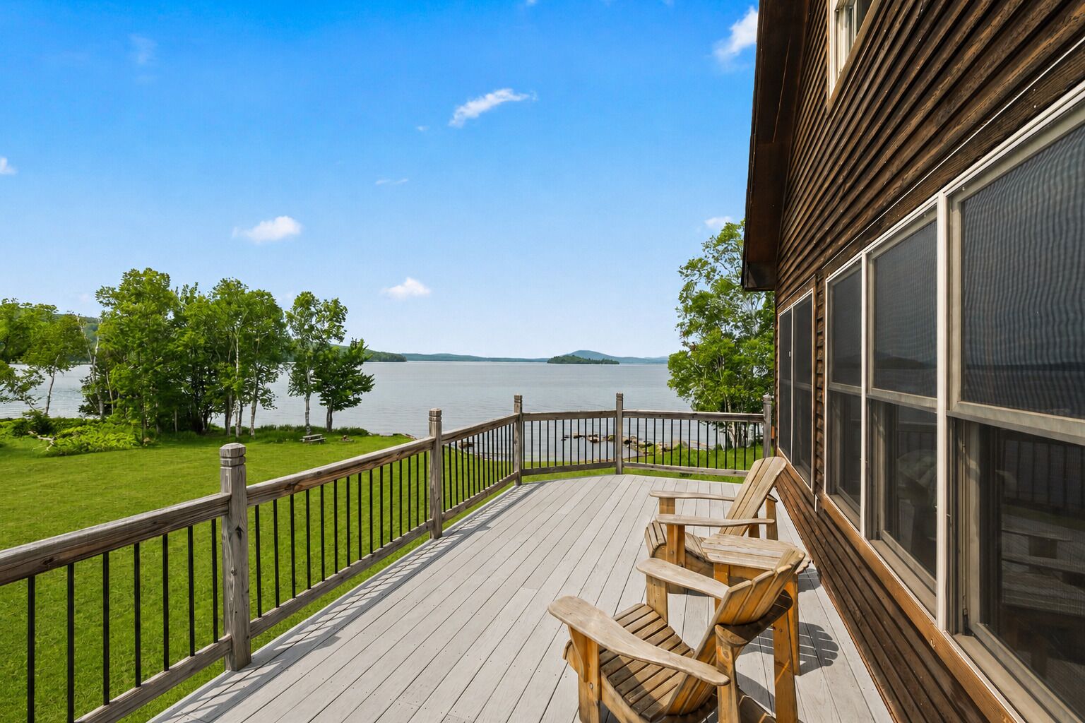 A wooden deck with a view of a lake, a wooden chair, and a building with large windows.