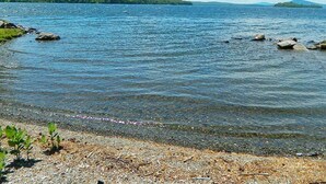 A lake with clear water, surrounded by a rocky shoreline and distant green hills. - Rangeley Lake Lodge - On Rangeley Lake with large lawn and close to town! (Rangeley)