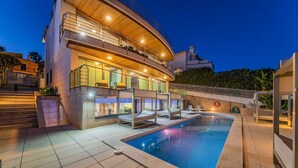 En moderne bygning med to etager, en swimmingpool, udendørs siddepladser og en godt oplyst balkon.