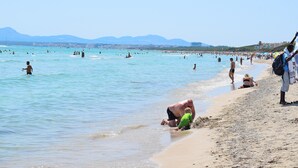 En overfyldt strand med folk, der svømmer og går langs kysten.