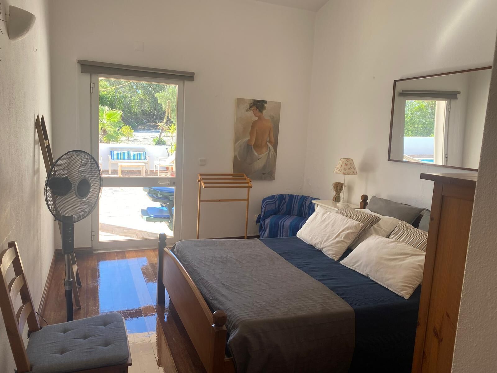Une chambre à coucher avec un lit, une chaise, un ventilateur, un tableau et une vue sur l’extérieur.
