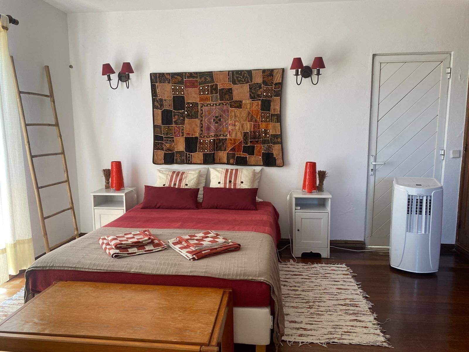 A bedroom with a bed, two bedside tables, a wall hanging, a heater, and a wooden bench.