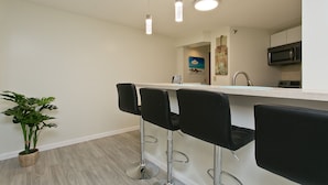 Een moderne keuken met een wit aanrecht, roestvrijstalen apparatuur en zwarte barstoelen.