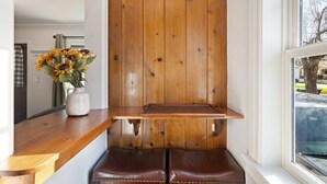 A wooden bench with a white wall behind it, a window to the right, and a vase with sunflowers on a wooden table to the left. - Perfect Couples Getaway! Walk to Dwntwn, Galveston Corridor & Drake Park, Parking, Air Conditioning (Bend)