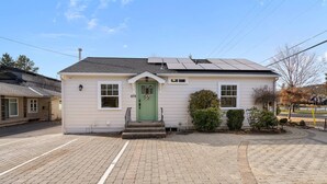A single-story house with a green door, solar panels on the roof, and a paved driveway. - Perfect Couples Getaway! Walk to Dwntwn, Galveston Corridor & Drake Park, Parking, Air Conditioning (Bend)