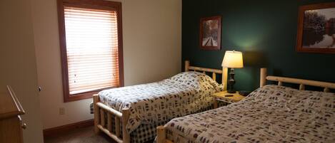 A room with two wooden beds, a ceiling fan, a window with blinds, and two wall-mounted lamps.
