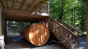 Une terrasse en bois avec une grande barrique, un escalier et un mur en pierre.