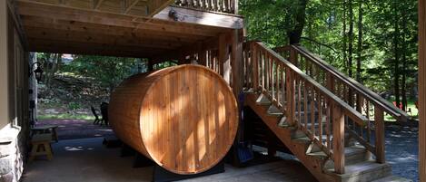 Una terraza de madera con un barril grande, una escalera y un muro de piedra.