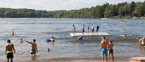 A beach scene with people swimming and standing on a dock.
