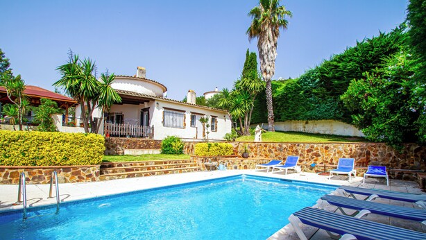Une piscine avec des chaises longues, un mur en pierre et une maison dotée d’un balcon.