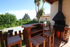 An outdoor patio with wooden tables and chairs, a built-in grill, and a view of greenery. - Club Villamar - Beautiful villa with  private pool and nice garden (Calonge)