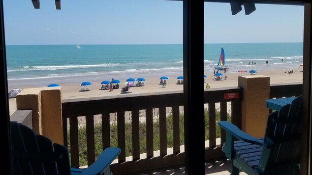 A beach view from a covered area with chairs and umbrellas.