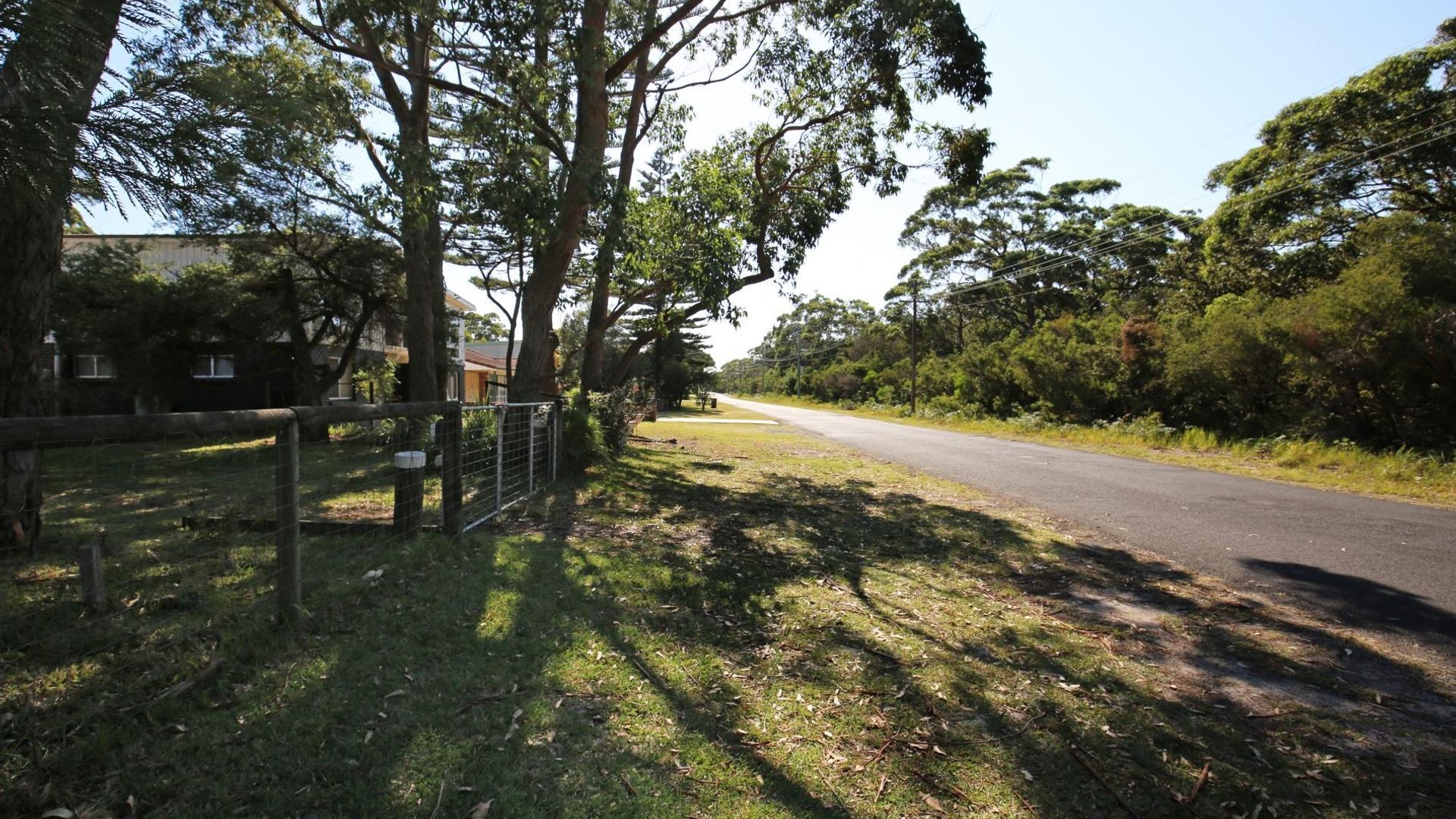 A rural road flanked by trees and a fence.