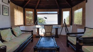 Un espace extérieur abrité, aménagé avec une table et des chaises, un trépied et des œuvres d’art encadrées accrochées aux murs.